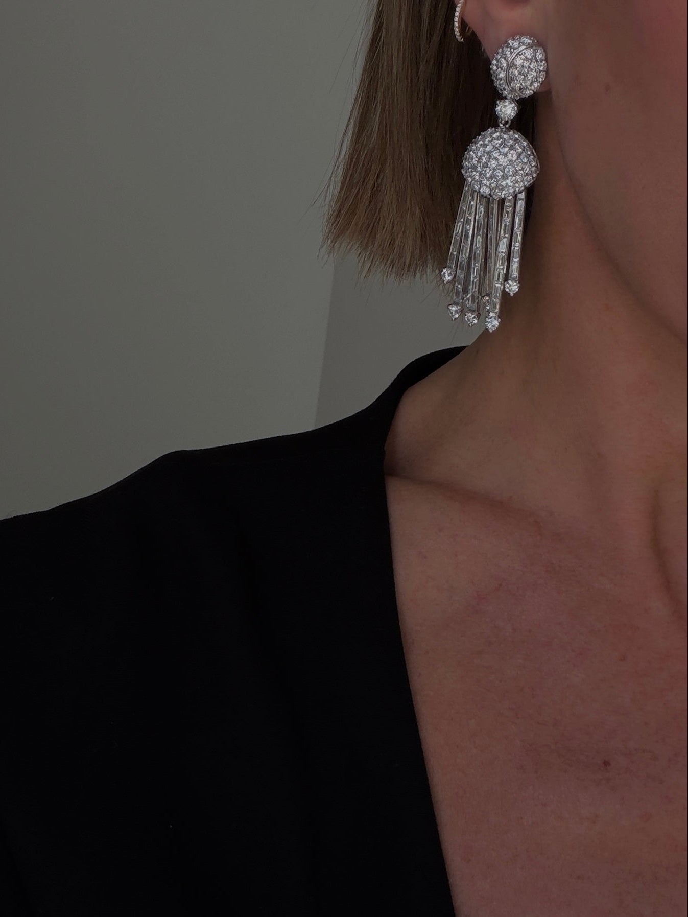 Close-up of a person wearing sparkling earrings against a neutral background