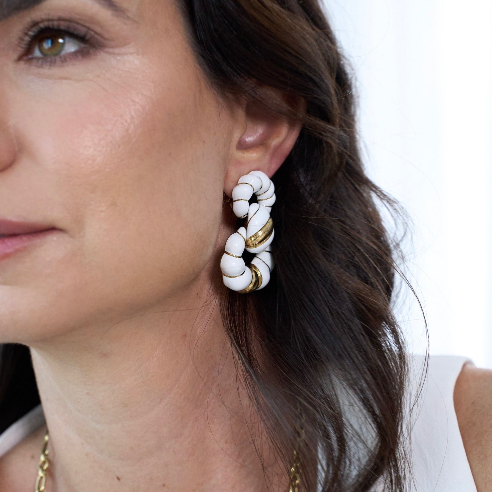 Close-up of a woman wearing white and gold earrings with a blurred background