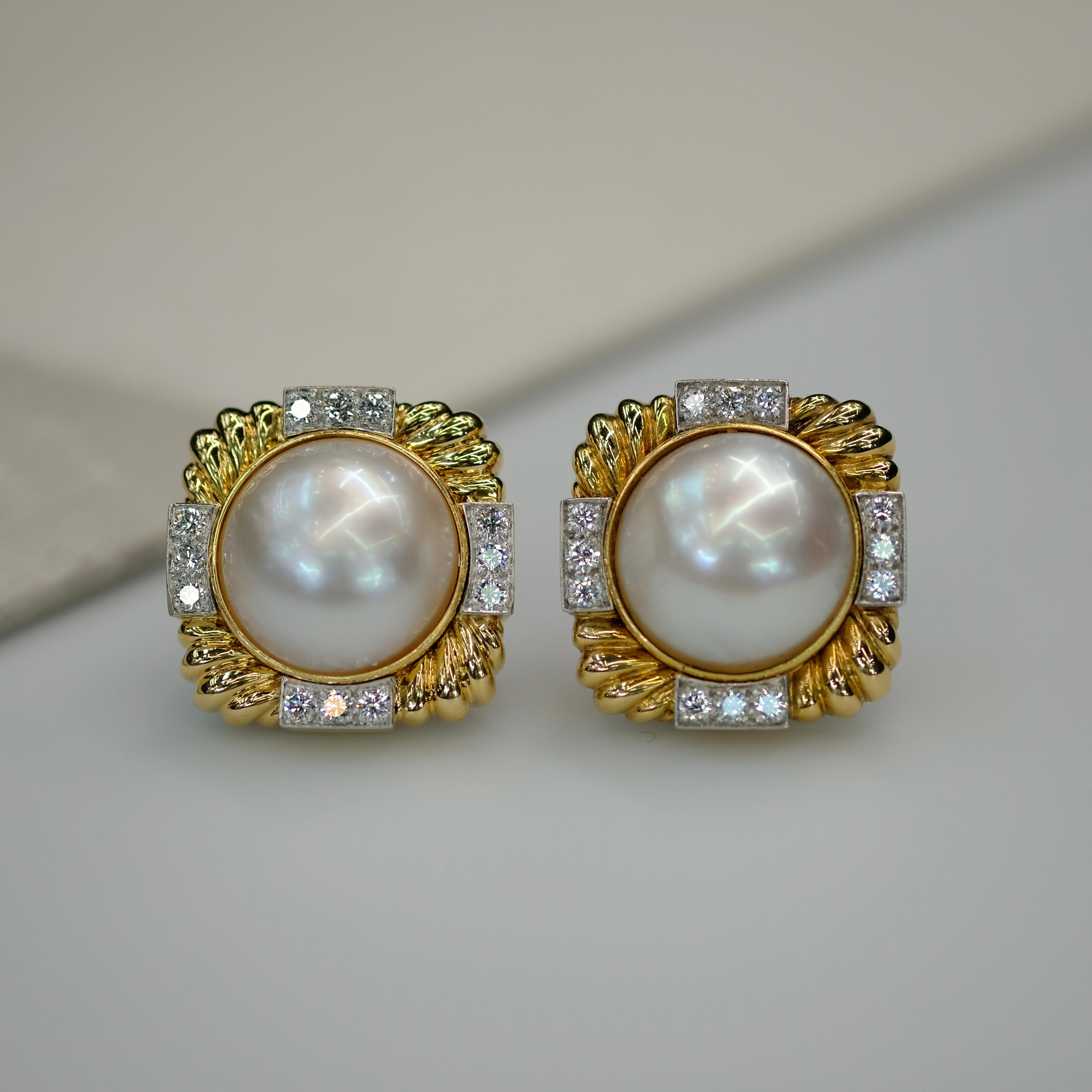 Pair of pearl earrings with gold and diamond accents on a light background. David Webb.