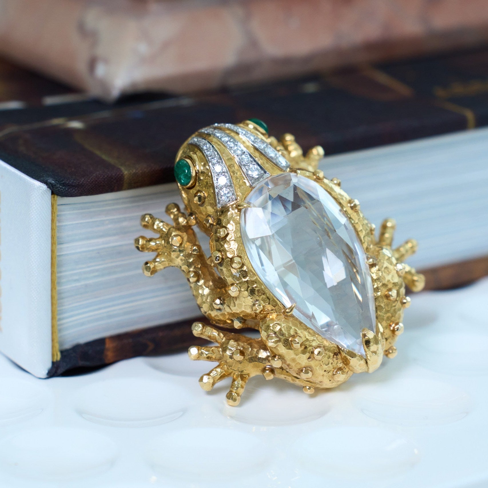 Gold frog-shaped David Webb brooch with a large gemstone on a book