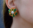 Close-up of an ear wearing a decorative earring with green, orange, and pearl details.