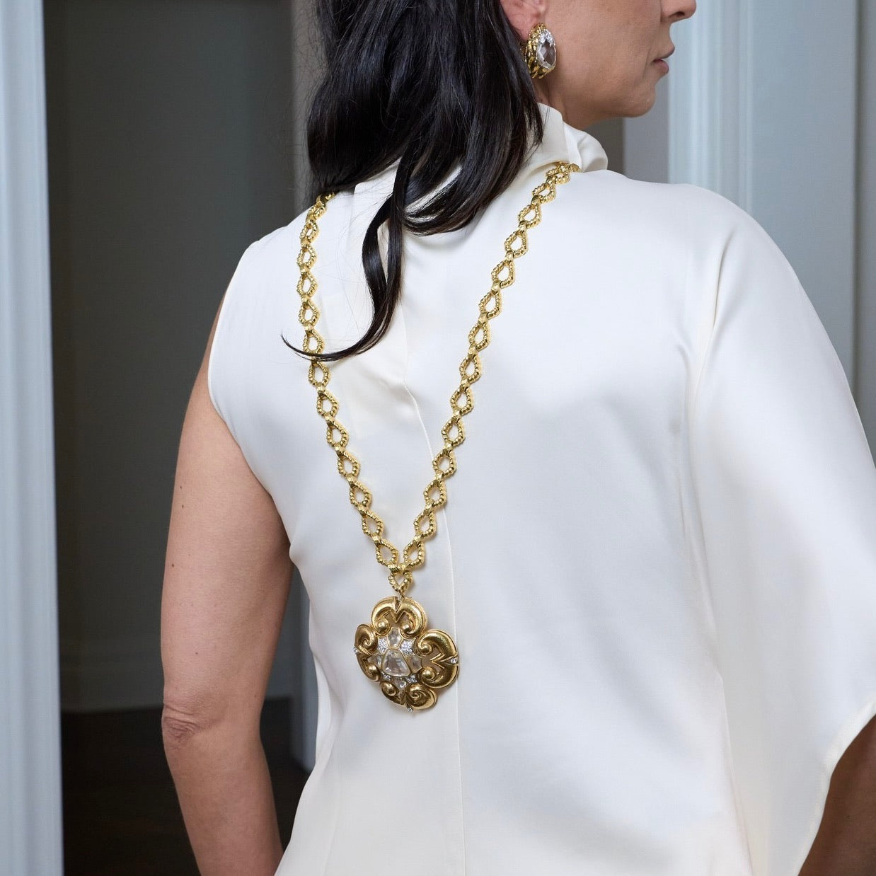 Woman wearing a gold chain David Webb necklace with a large pendant.