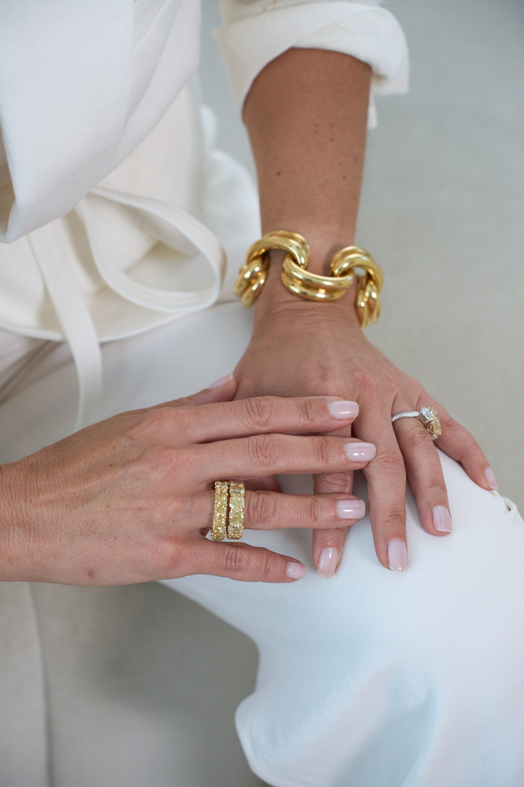 Close-up of hands wearing gold bracelets and rings on a white background